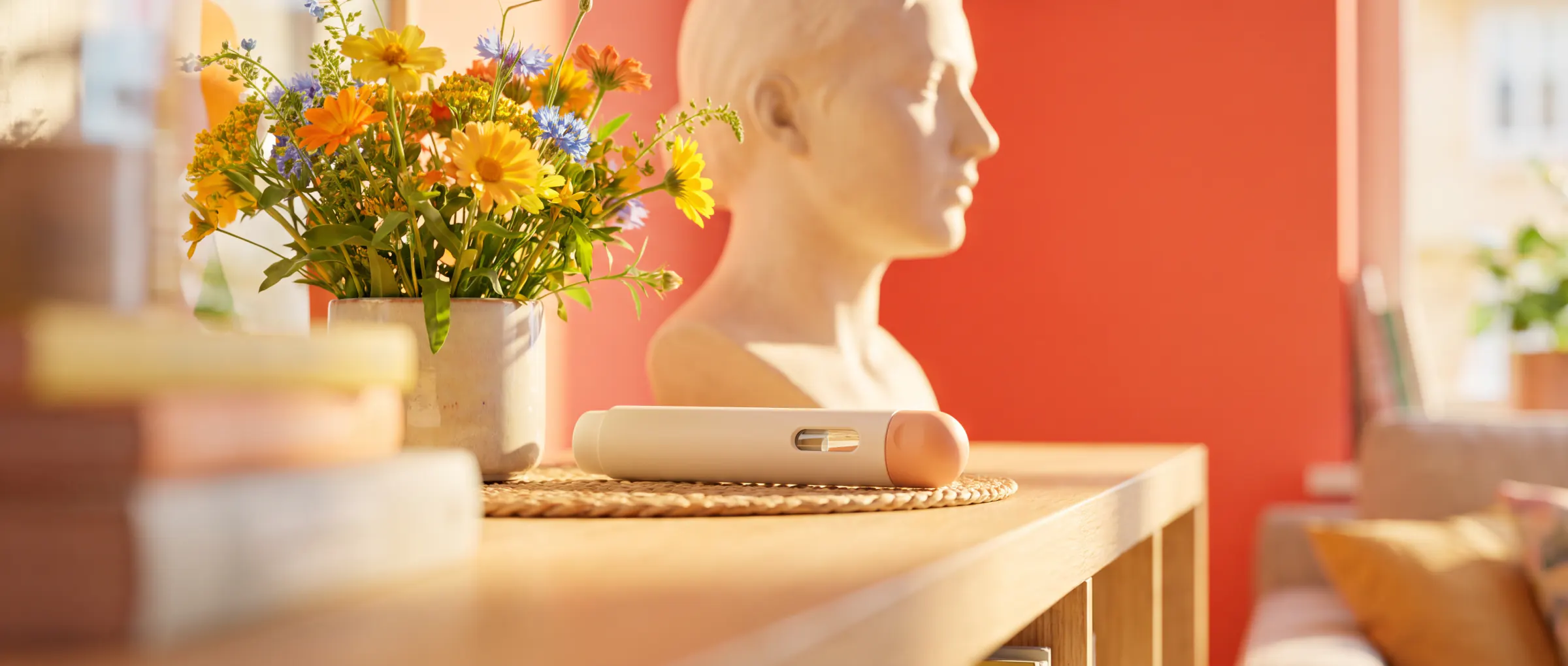 A pale plaster bust in profile on a sunny shelf beside a plain injection pen and flowers